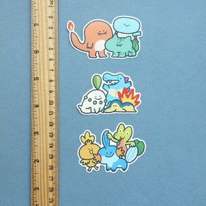 May include: Three sets of colourful cartoon stickers featuring various Pokemon characters. The stickers are on a blue background with a ruler for scale.