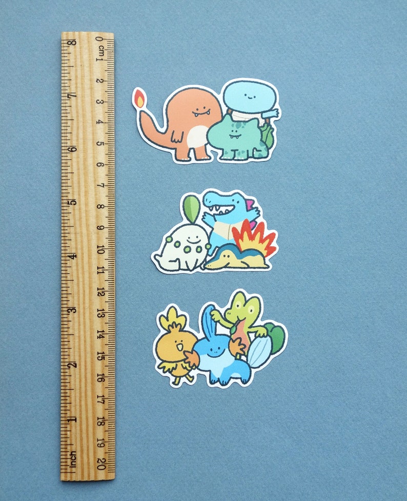 May include: Three sets of colourful cartoon stickers featuring various Pokemon characters. The stickers are on a blue background with a ruler for scale.