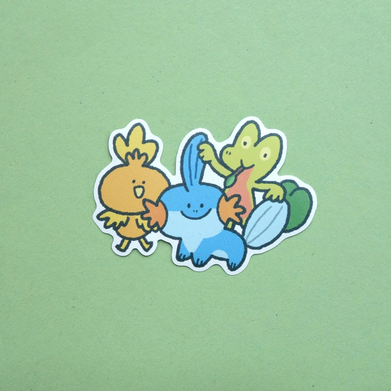 May include: A sticker featuring three cartoon characters: a yellow chick, a blue and orange sea creature, and a green frog. The chick is holding the sea creature's hand, and the frog is holding a leaf.