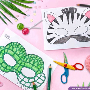 K&ouml;nnte beinhalten: Zwei Ausmalbilder mit Umrissen von Tiermasken, eines mit Zebra- und das andere mit Krokodilmuster, werden mit Buntstiften und einer Schere gezeigt. Die Zebramaske ist schwarz-wei&szlig; und die Krokodilmaske ist gr&uuml;n. Der Hintergrund ist rosa.
