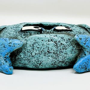 May include: A whimsical, handcrafted crab figurine in shades of blue. The crab has a textured body and bright blue claws. The eyes are white with black accents. This decorative item is perfect for coastal decor.