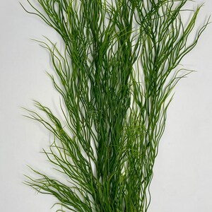 May include: A bundle of artificial green grass stems with a naturalistic appearance. The stems are long, thin, and slightly curved, creating a flowing, textured look. The grass is a vibrant green color, suitable for decorative purposes.