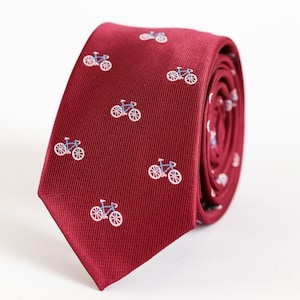 May include: A burgundy necktie with a repeating pattern of white bicycles. The tie is rolled up and the pattern is visible on the front and back of the tie.