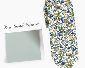 Può includere: Una cravatta bianca con un motivo floreale in tonalità di blu, verde e arancio. La cravatta ha una punta a punta e  è realizzata in un morbido tessuto di cotone. "Dress Swatch Reference" è scritto su una carta bianca con un campione verde chiaro.