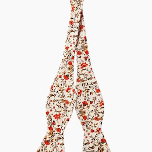 May include: A white bow tie with a floral pattern featuring red flowers and brown stems.