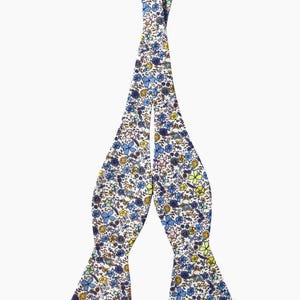 Pode incluir: Uma gravata borboleta branca com um padrão floral em tons de azul, amarelo e rosa.