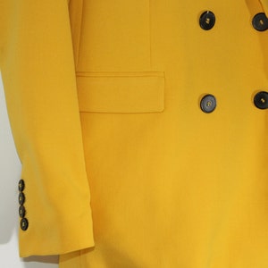 Puede incluir: Una chaqueta amarilla de doble botonadura con botones negros.