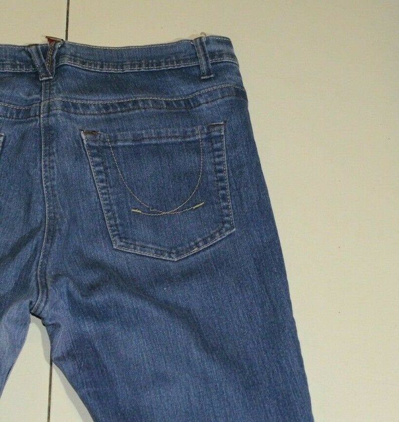 Puede incluir: Un par de pantalones vaqueros azules con un bolsillo trasero. El bolsillo tiene un detalle de costura curvado.