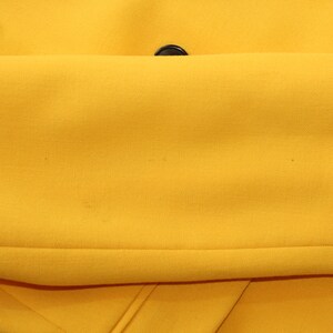 Puede incluir: Una chaqueta amarilla con botones negros. La chaqueta est&aacute; doblada por la mitad, mostrando el interior de la tela.