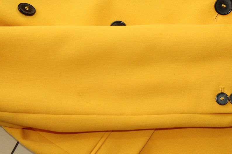 Puede incluir: Una chaqueta amarilla con botones negros. La chaqueta est&aacute; doblada por la mitad, mostrando el interior de la tela.