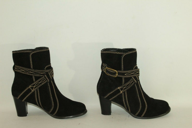 Pode incluir: Um par de botas de tornozelo de camur&ccedil;a preta com costuras douradas e um detalhe de fivela. As botas t&ecirc;m um salto bloco.