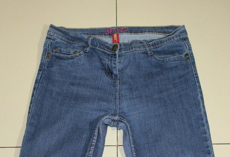 Puede incluir: Un par de pantalones vaqueros azules con una etiqueta rosa "Spring" en la cintura.