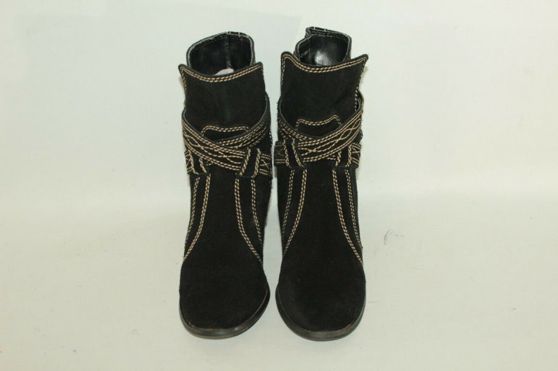 Pode incluir: Um par de botas de tornozelo de camur&ccedil;a preta com detalhes de costura dourada. As botas t&ecirc;m um salto baixo e uma ponta pontiaguda.