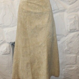 May include: A light beige suede skirt with a slightly flared silhouette. The skirt has a simple design and a smooth texture.