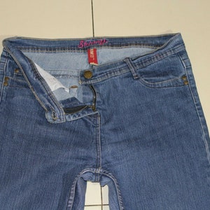 Puede incluir: Un par de pantalones vaqueros azules de mezclilla con cierre de cremallera y bot&oacute;n. La cintura tiene una etiqueta rosa que dice "Sears".