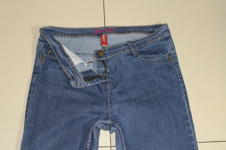 Puede incluir: Un par de pantalones vaqueros azules de mezclilla con cierre de cremallera y bot&oacute;n. La cintura tiene una etiqueta rosa que dice "Sears".