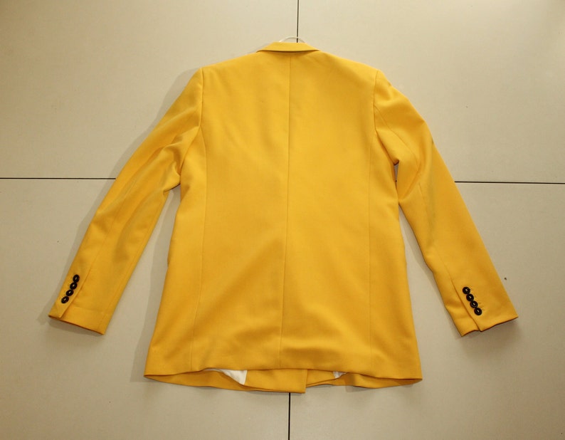 Puede incluir: Una chaqueta amarilla brillante con botones negros en las mangas.