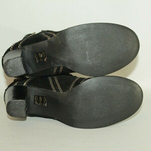 Pode incluir: Um par de botas de tornozelo de camur&ccedil;a preta com costuras douradas e salto bloco. As botas t&ecirc;m sola de borracha.