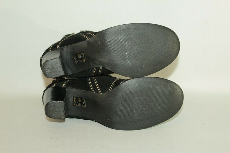 Pode incluir: Um par de botas de tornozelo de camur&ccedil;a preta com costuras douradas e salto bloco. As botas t&ecirc;m sola de borracha.