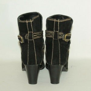 Pode incluir: Botas de tornozelo de camur&ccedil;a preta com fivela dourada e costuras decorativas. As botas t&ecirc;m um salto bloco.