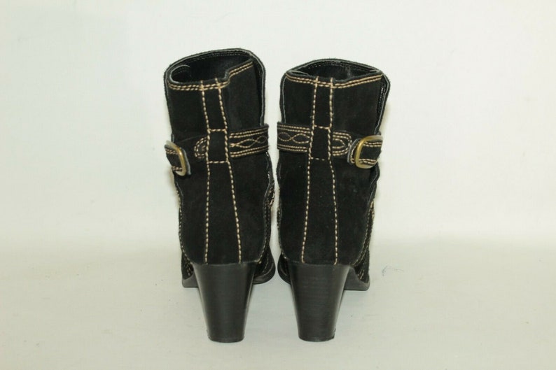 Pode incluir: Botas de tornozelo de camur&ccedil;a preta com fivela dourada e costuras decorativas. As botas t&ecirc;m um salto bloco.