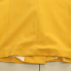 Puede incluir: Una chaqueta amarilla con mangas largas y un cierre de bot&oacute;n &uacute;nico. La chaqueta est&aacute; hecha de una tela lisa y tejida.