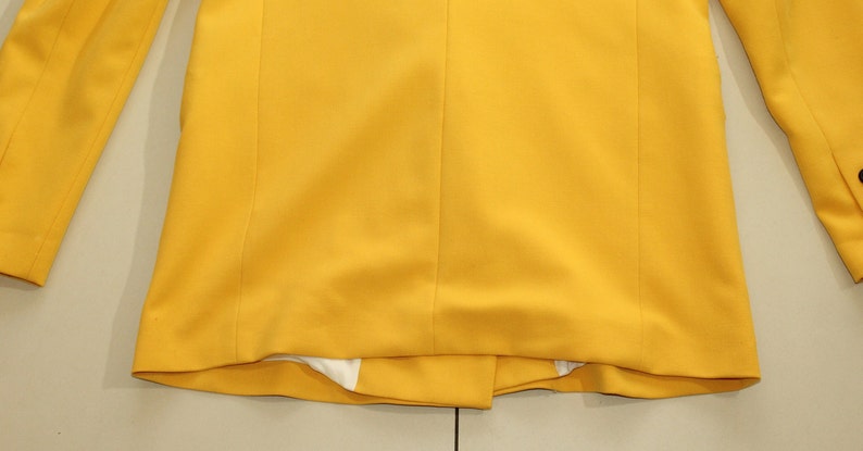 Puede incluir: Una chaqueta amarilla con mangas largas y un cierre de bot&oacute;n &uacute;nico. La chaqueta est&aacute; hecha de una tela lisa y tejida.