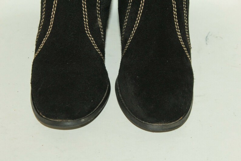 Pode incluir: Um par de botas de tornozelo de camur&ccedil;a preta com costuras douradas. As botas t&ecirc;m uma ponta arredondada e um salto baixo.