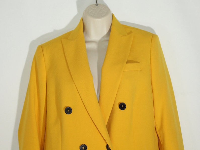 Puede incluir: Una chaqueta amarilla brillante de doble botonadura con botones negros.