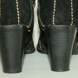 Pode incluir: Um par de botas de salto alto de camur&ccedil;a preta com detalhes de costura branca. As botas t&ecirc;m um salto bloco e uma ponta pontiaguda.