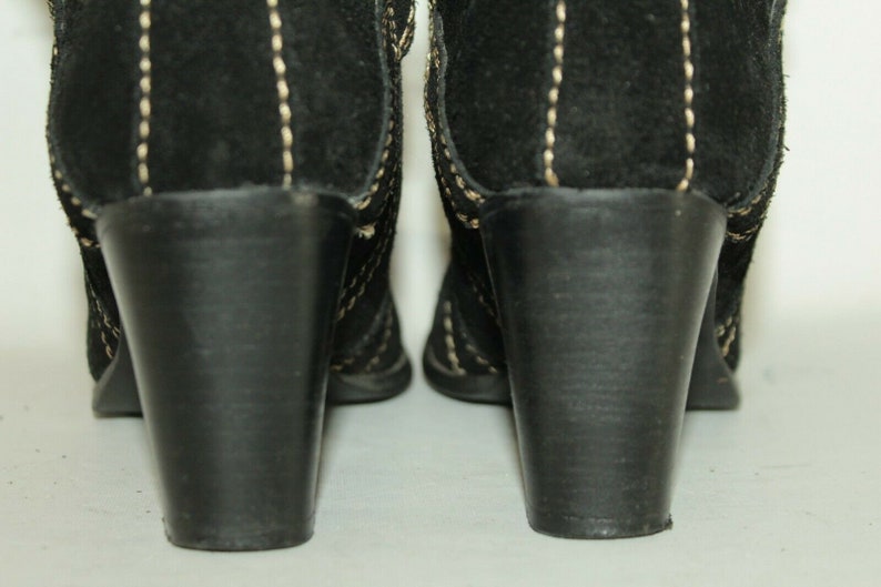 Pode incluir: Um par de botas de salto alto de camur&ccedil;a preta com detalhes de costura branca. As botas t&ecirc;m um salto bloco e uma ponta pontiaguda.