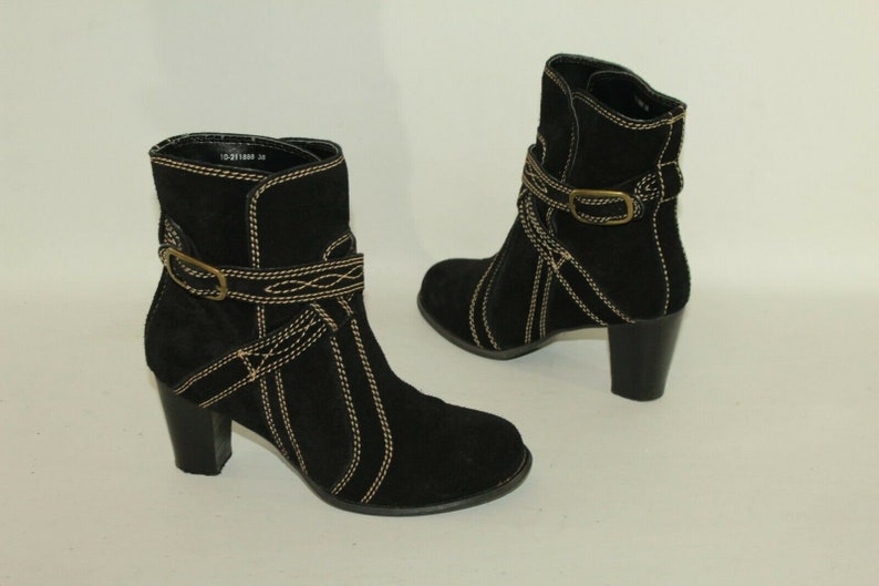 Pode incluir: Botas de tornozelo de camur&ccedil;a preta com fivela dourada e detalhes de costura. As botas t&ecirc;m um salto bloco.