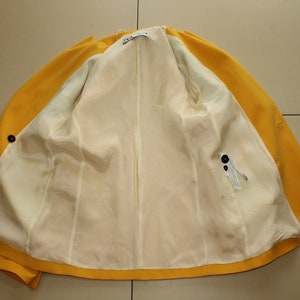 Puede incluir: Una chaqueta amarilla con forro blanco. La chaqueta tiene cierre de bot&oacute;n y un bolsillo en el lado derecho.