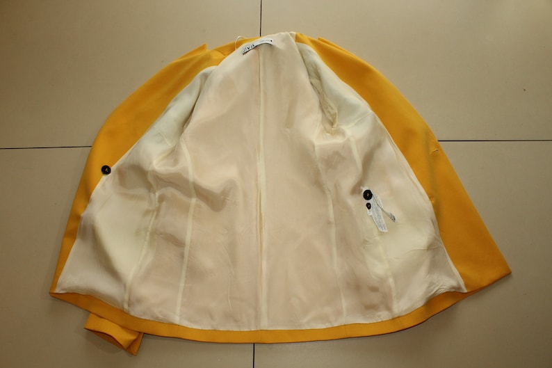 Puede incluir: Una chaqueta amarilla con forro blanco. La chaqueta tiene cierre de bot&oacute;n y un bolsillo en el lado derecho.