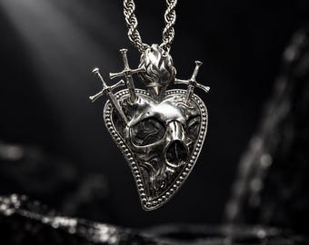 May include: A silver-toned pendant necklace featuring a heart-shaped design with a central skull motif. The pendant is pierced by three small swords and topped with a flame-like element, all suspended from a thick, twisted rope-style chain.