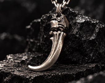 May include: A silver-toned pendant shaped like a curved claw with a textured, weathered surface. The top of the claw features a mechanical, gear-like metal cap with visible screws, suspended from a thick, interlocking silver-toned metal chain.