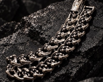 May include: A silver-toned metal bracelet featuring a chain design composed of interconnected bone-like links. The clasp is shaped like a detailed human skull, providing a secure closure for this heavy-duty link bracelet.
