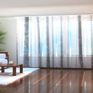 Op de afbeelding: Een witte bank met kussens staat in een woonkamer met een houten salontafel en een wit tapijt. De kamer heeft grote ramen met transparante gordijnen met een bosprint.