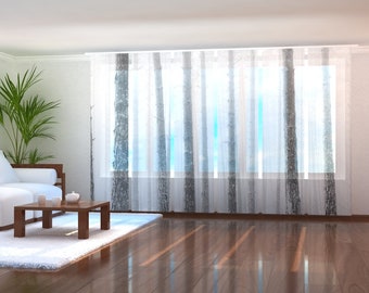 May include: A white couch with pillows sits in a living room with a wooden coffee table and a white rug. The room has large windows with sheer curtains featuring a forest print.