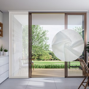 Puede incluir: Panel de cortina blanca y transparente colgado en una ventana con vista a un césped verde y árboles. La cortina está hecha de una tela ligera que permite que la luz se filtre.