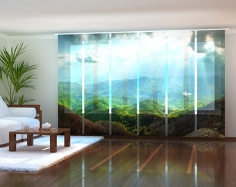 May include: A living room with a white sofa and a wooden coffee table. The window is covered with sheer curtains featuring a scenic mountain landscape with a bright blue sky and white clouds.