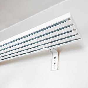 Può includere: Mensola in metallo bianco con quattro binari paralleli e una staffa in metallo bianco. La mensola è montata su una parete bianca.