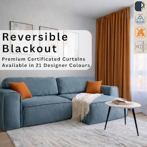 Op de afbeelding: Een woonkamer met een blauwe bank, oranje kussens en een witte deken. Een kleine tafel met een boek staat naast de bank. De tekst op de afbeelding luidt "Reversible Blackout" en "Premium Certificated Curtains Available in 21 Designer Colours." De gordijnen zijn oranje.