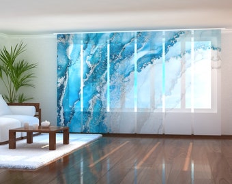 May include: Blue and white abstract patterned window curtains with a white sofa and a wooden coffee table in the foreground.