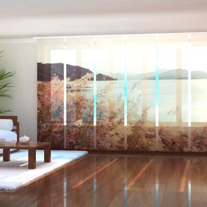 Op de afbeelding: Een woonkamer met een witte bank en een houten salontafel. Het raam heeft transparante gordijnen met een landschapsdruk van een meer en bergen.