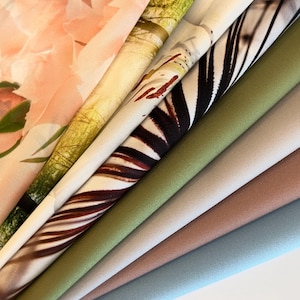 Op de afbeelding: Een verzameling stofstalen in verschillende kleuren en patronen, waaronder bloemen, zebraprint en effen kleuren. De stalen zijn in een waaier vorm gerangschikt, met de bloemenstof bovenaan en de effen kleuren onderaan.
