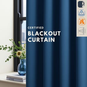 May include: A navy blue blackout curtain with the text "CERTIFIED BLACKOUT CURTAIN" in white. The curtain is next to a window with a vase of flowers and a stack of books. The window frame is black.