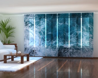 May include: White curtains with a blue and white ocean wave pattern. The curtains are hung in a living room with a white sofa and a wooden coffee table.