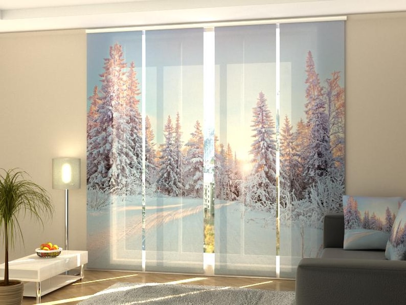 May include: Panel curtains with a winter wonderland scene.  The translucent panels depict a snowy forest path at sunrise, with snow-covered pine trees and a soft, light-blue sky.  The curtains are ideal for adding a serene, wintry ambiance to any room.  The image shows the curtains hung in a living room setting, showcasing their light filtering capabilities and overall aesthetic appeal.