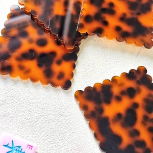 May include: Several tortoise shell patterned coasters with scalloped edges are scattered on a white surface. A pink Mahjong tile with blue Chinese characters is also visible. The coasters have a glossy finish.